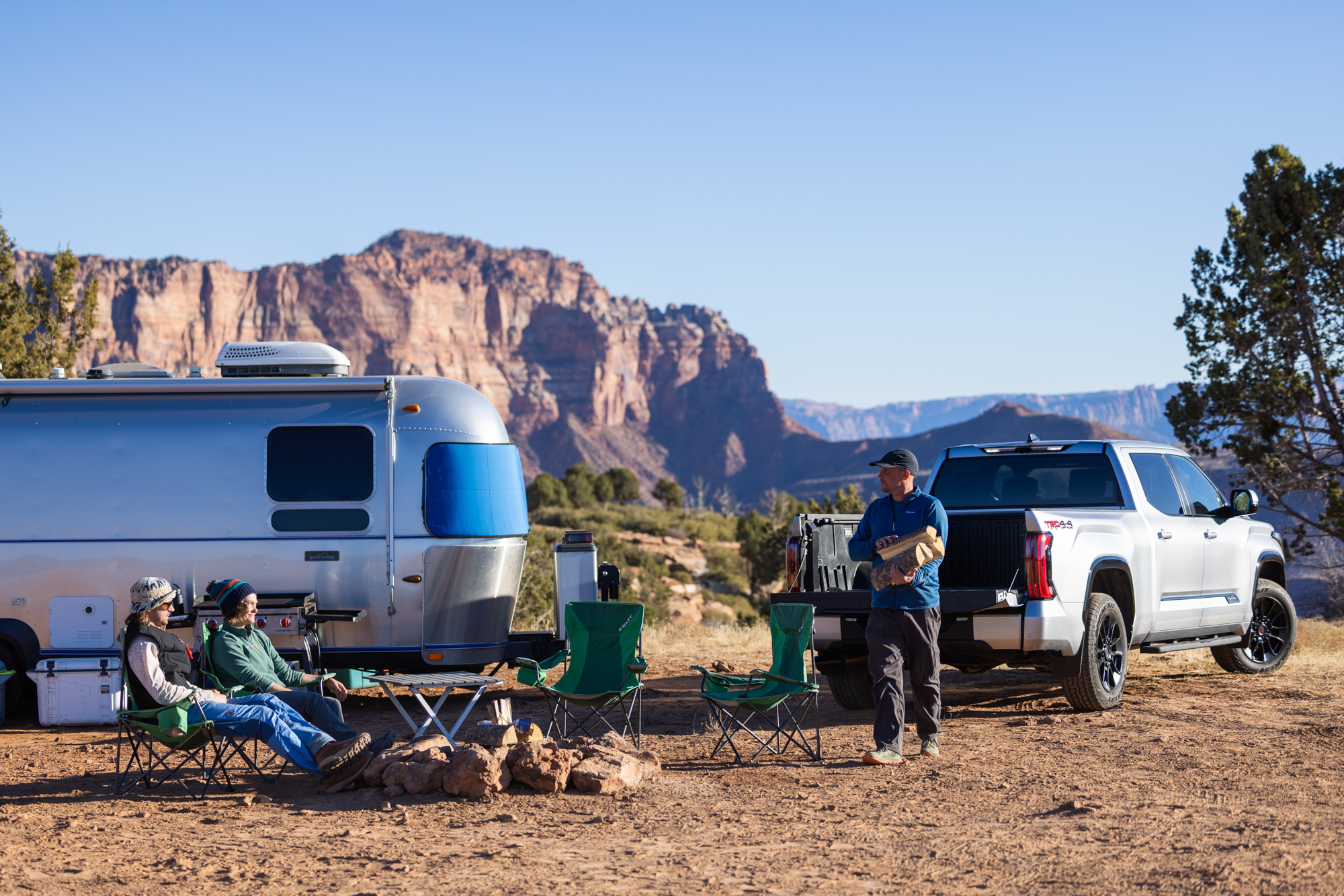 Airstream camp setup in the desert with crew around a fire ring