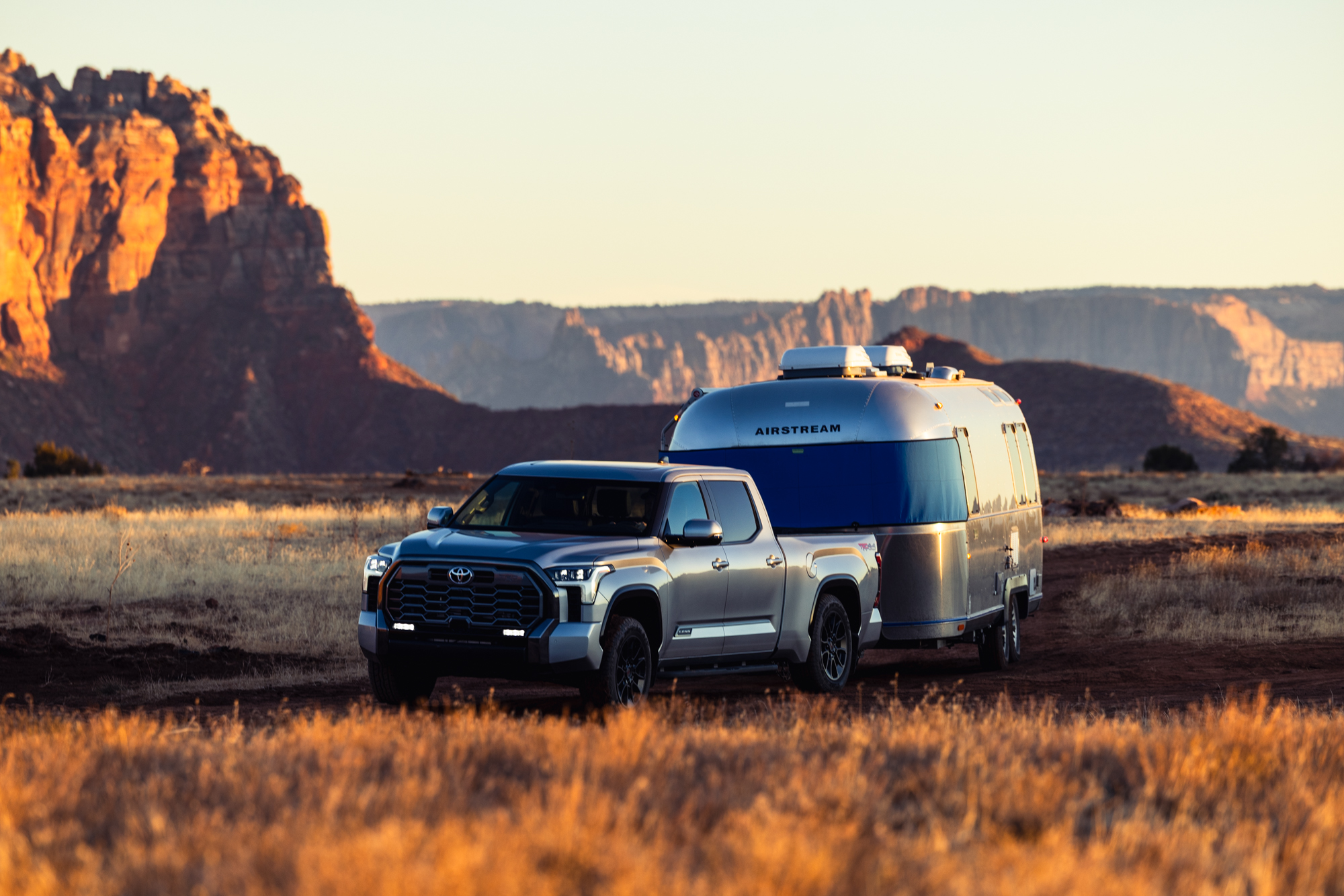 Airstream towed by a truck at golden hour with red rock cliffs