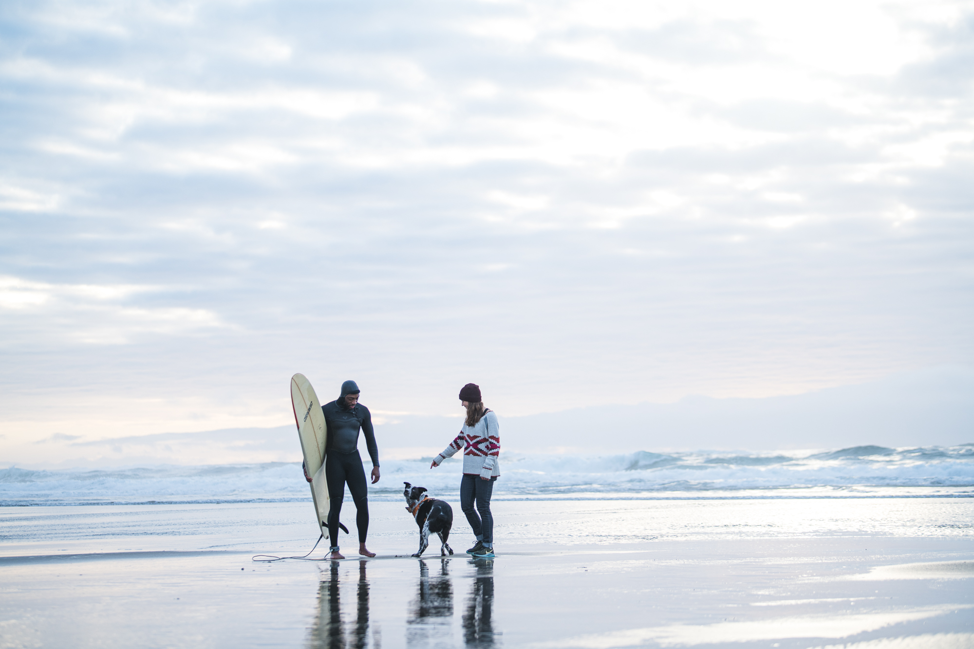 Surfer, woman and dog on a wide winter beach at dawn