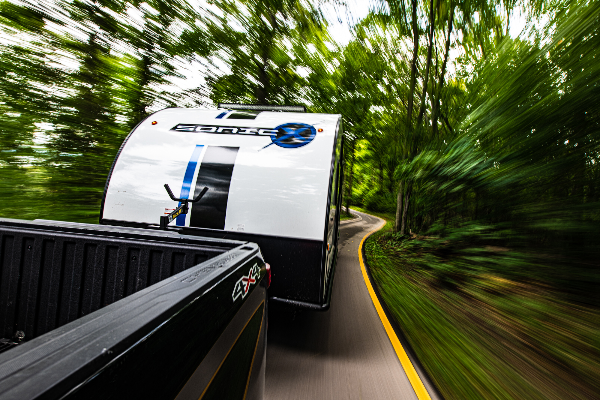 Travel trailer in motion on a tree-lined road, shot from a chase vehicle
